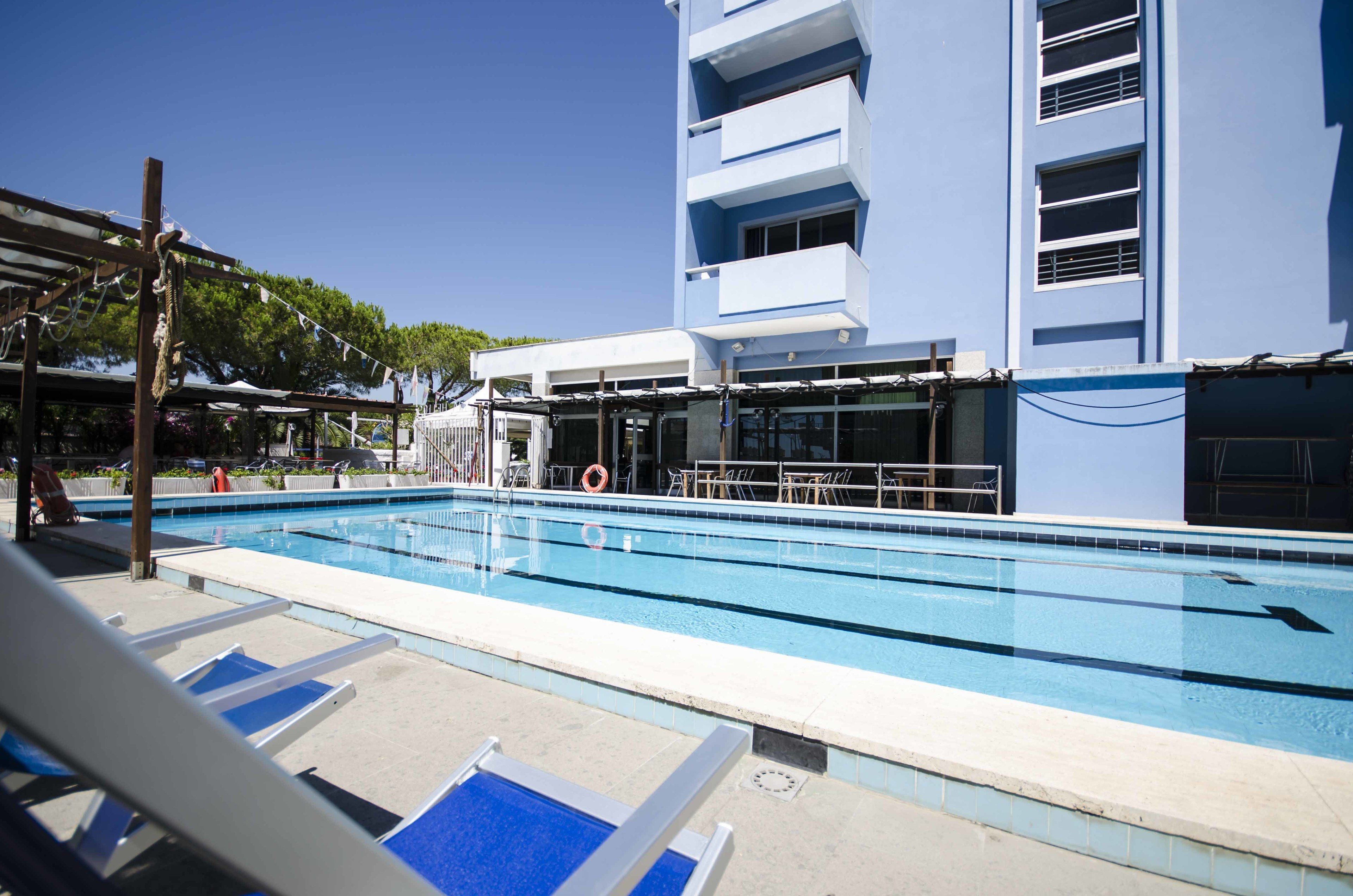 Una piscina con sillas de descanso y un edificio al fondo.