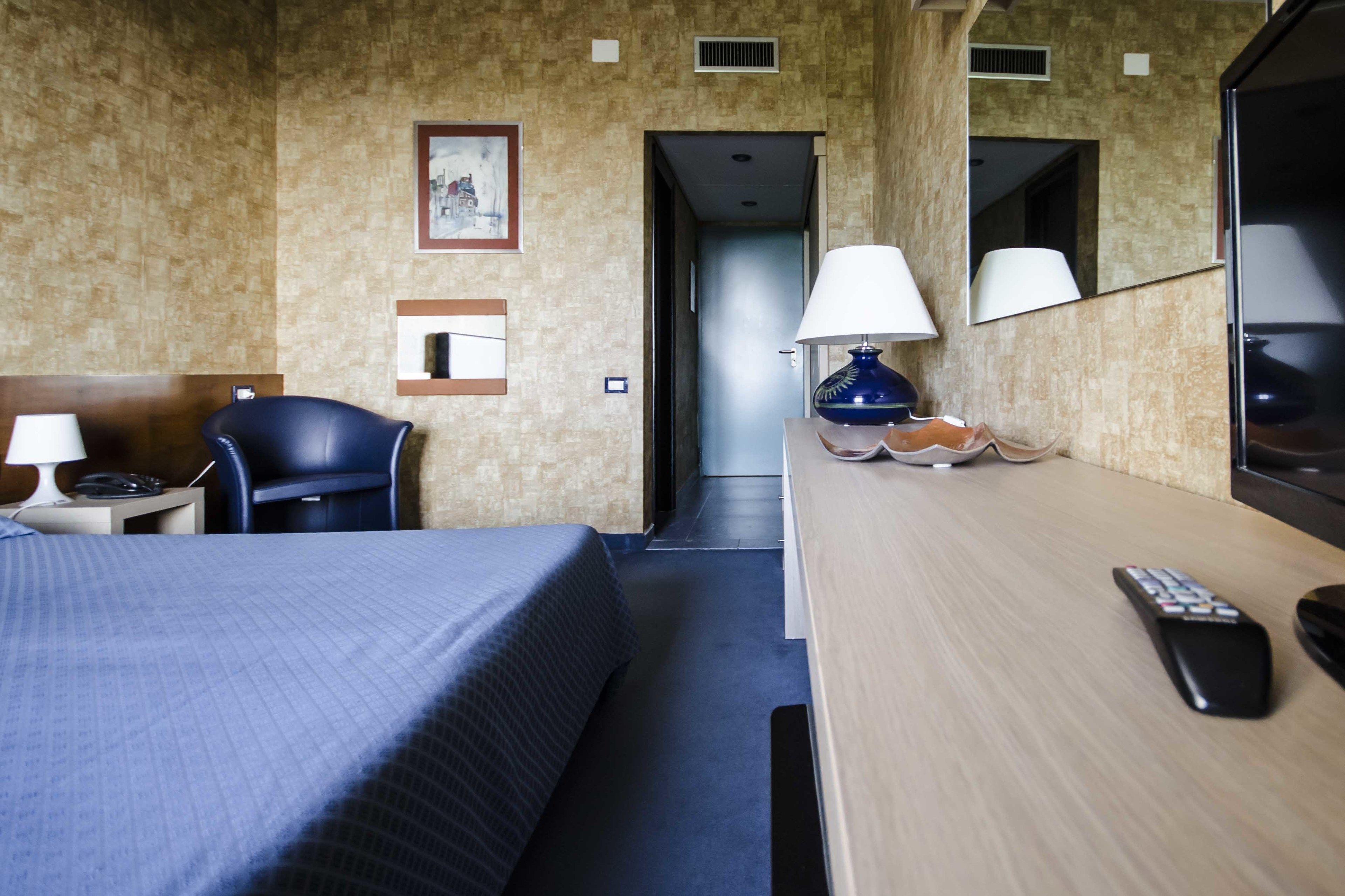A hotel room with a bed, a desk, a chair, a lamp, a remote control, and a mirror.
