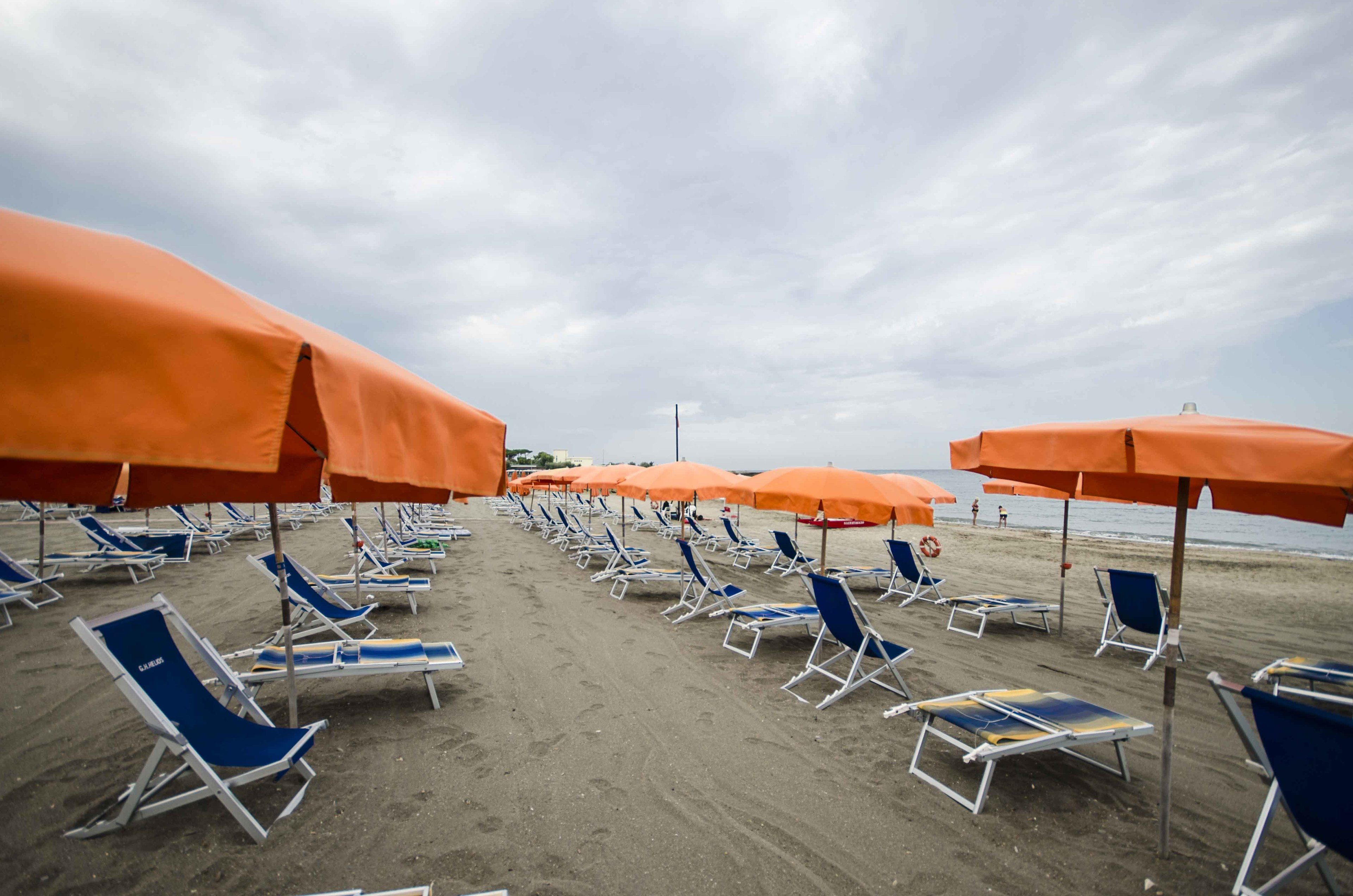 A beach with rows of blue and white sun loungers under orange umbrellas.