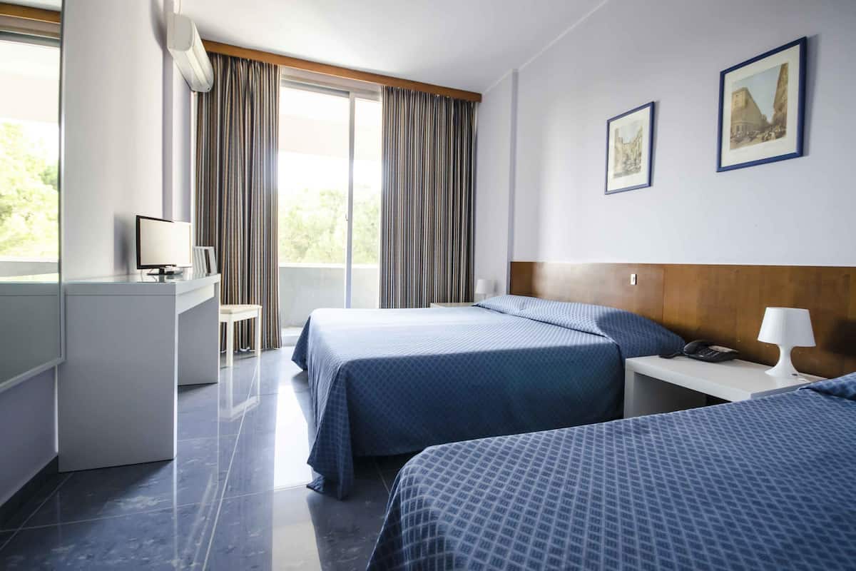 Une chambre d’hôtel avec deux lits, un bureau avec un ordinateur, une chaise et une fenêtre avec des rideaux.