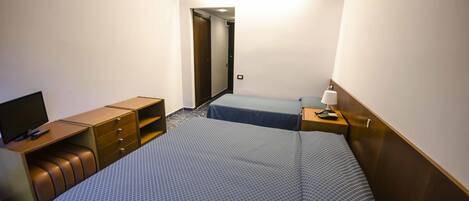 Habitación de hotel con cama, escritorio y silla, televisor y mesita de noche con lámpara.