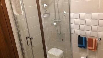 Un angolo doccia con porta in vetro, un lavandino bianco e una parete rivestita di piastrelle con un porta asciugamani.