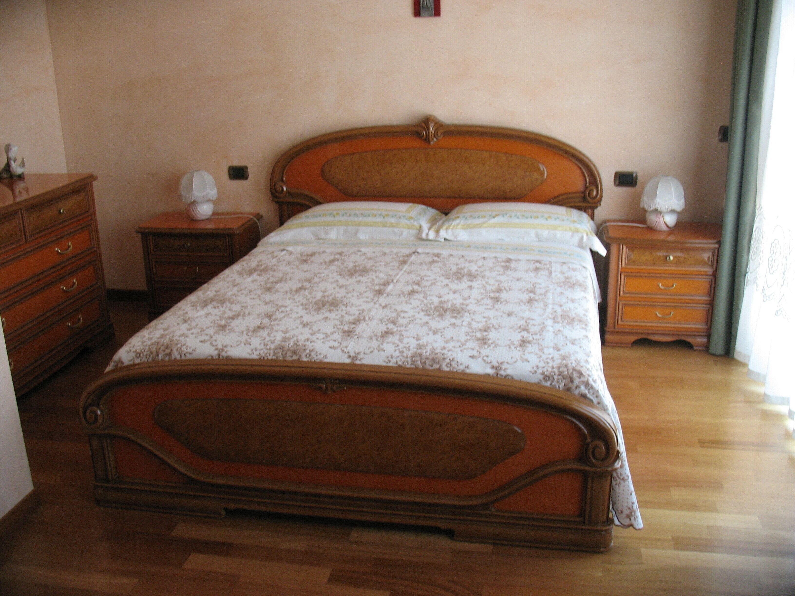 A bedroom with a wooden bed, two nightstands, a dresser, and a window with curtains.