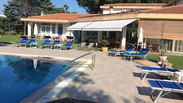 A pool area with lounge chairs and a building with a tiled roof.