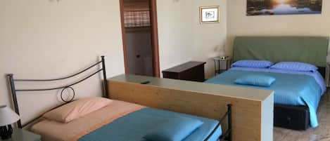 Un dormitorio con dos camas, un aparador de madera, una mesita de noche, una lámpara, un cuadro enmarcado y un equipo de aire acondicionado.