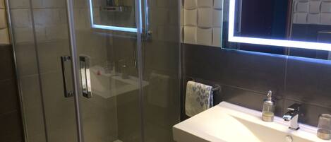 A modern bathroom with a glass-enclosed shower, a white sink, and a large mirror.