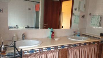 Un baño con dos lavabos, un espejo y una puerta que da a otra habitación.