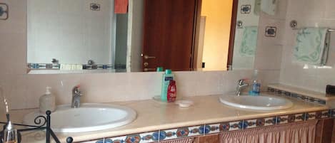 Un baño con dos lavabos, un espejo y una puerta que da a otra habitación.