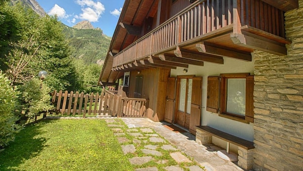 Een houten chalet met een gevel van natuursteen, een balkon en een pad van natuursteen dat naar de ingang leidt.