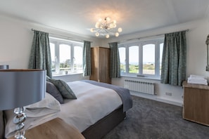 A bedroom with a large bed, a bedside table, a lamp, a wooden wardrobe, and a view through the windows.