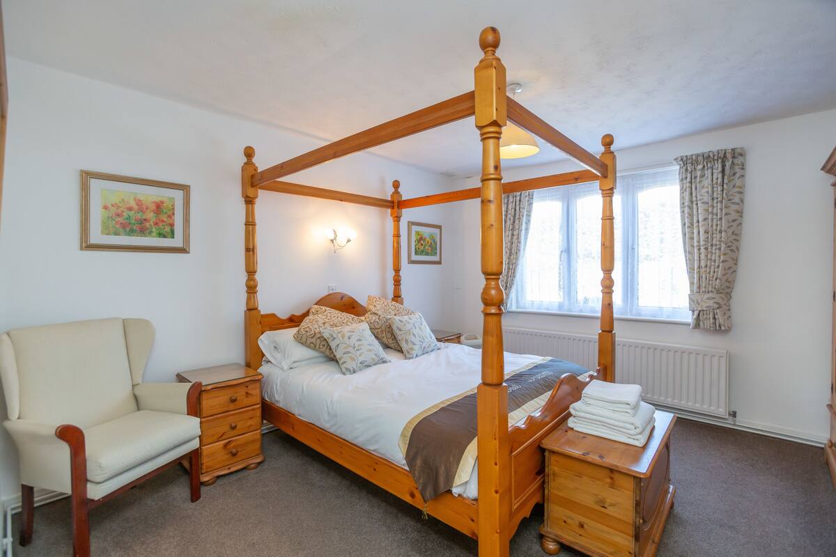 A four-poster bed with a wooden frame, a bedside table, a chair, and a radiator.