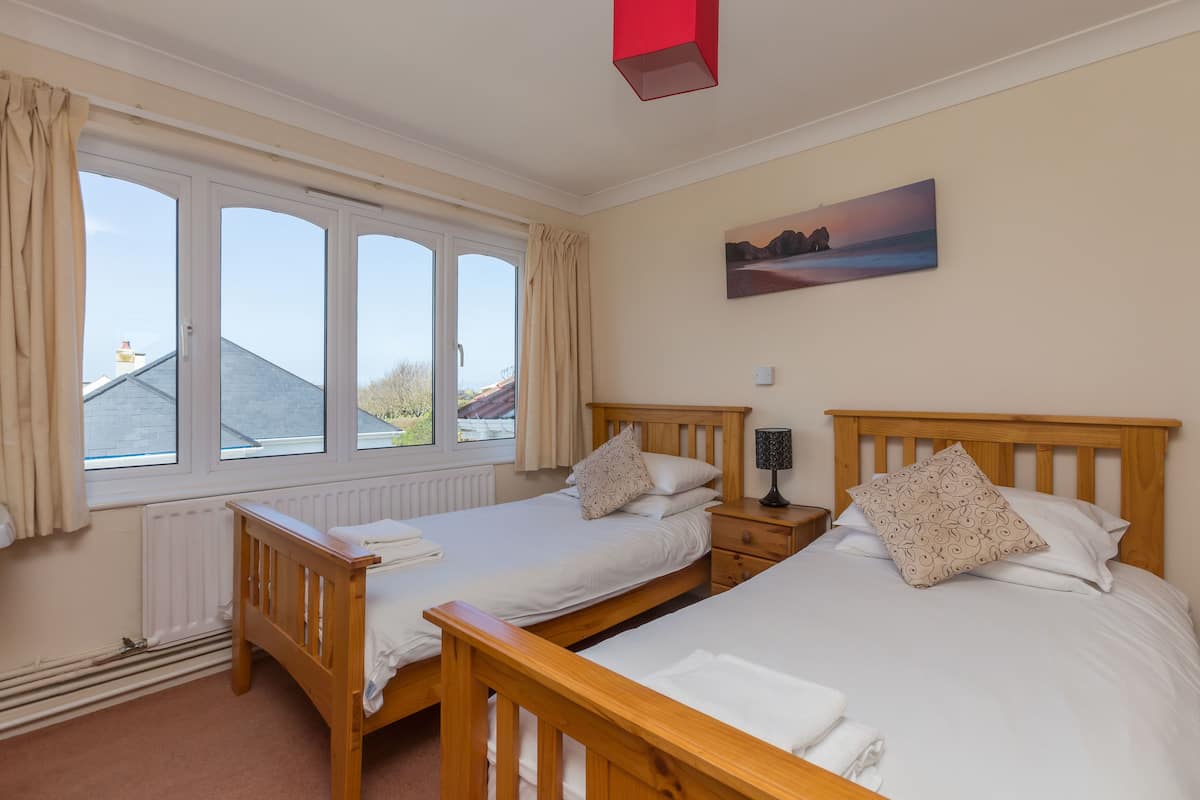A bedroom with two single beds, a wooden headboard, a nightstand with a lamp, and a window with curtains.