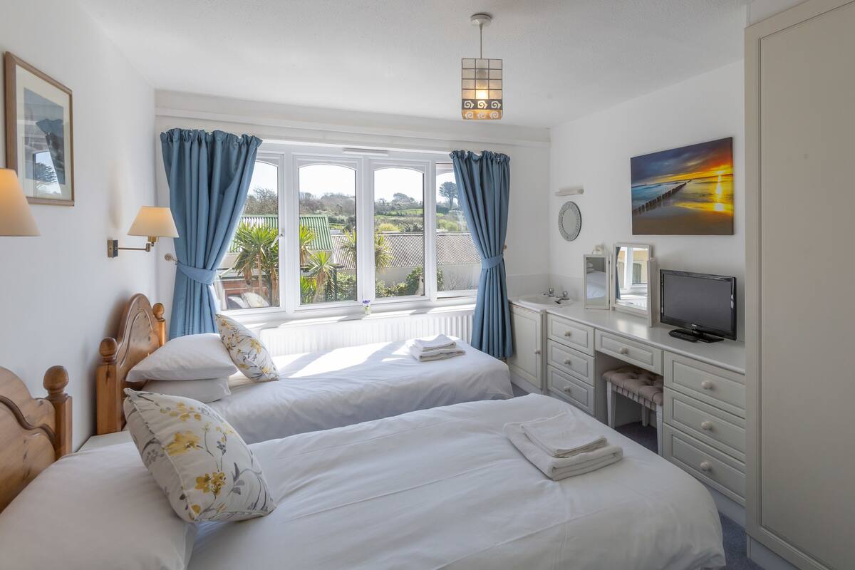 A hotel room with two beds, a television, a desk, and a view of the outdoors.