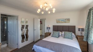 A bedroom with a large bed, bedside tables, a chandelier, a painting, and a door with a mirror. - Beau Vallon Holiday Apartments (St. Pierre du Bois)
