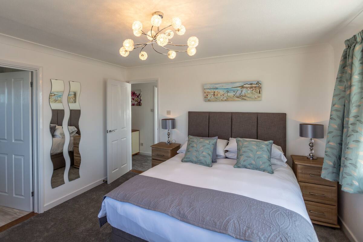 A bedroom with a large bed, bedside tables, a chandelier, a painting, and a door with a mirror.