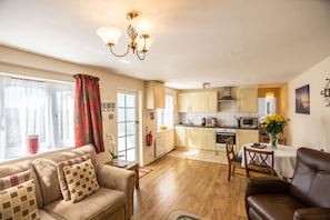 A living room with a sofa, a dining table, and a kitchen in the background.