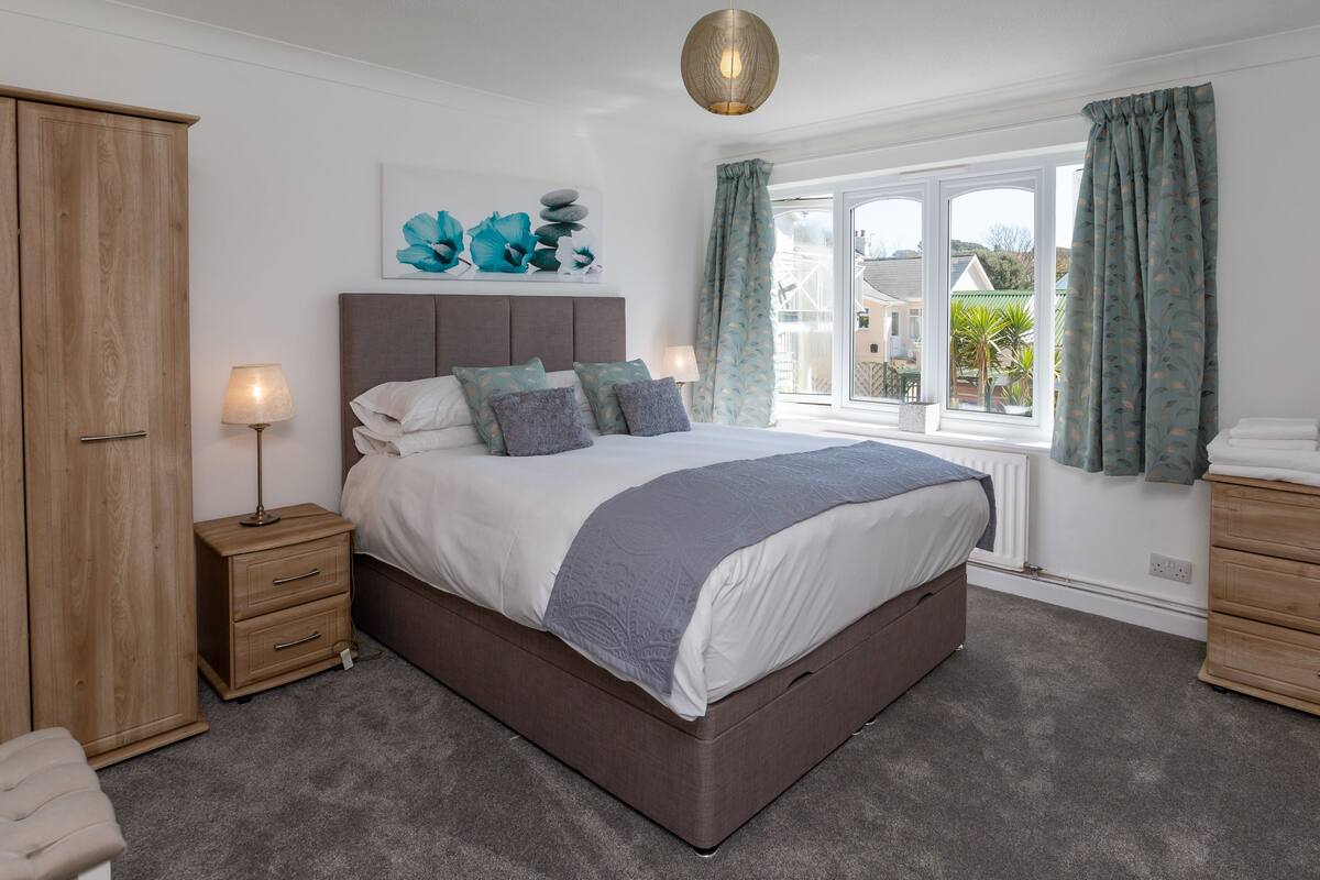 A bedroom with a large bed, wooden wardrobe, bedside tables, a television, and a window with curtains.