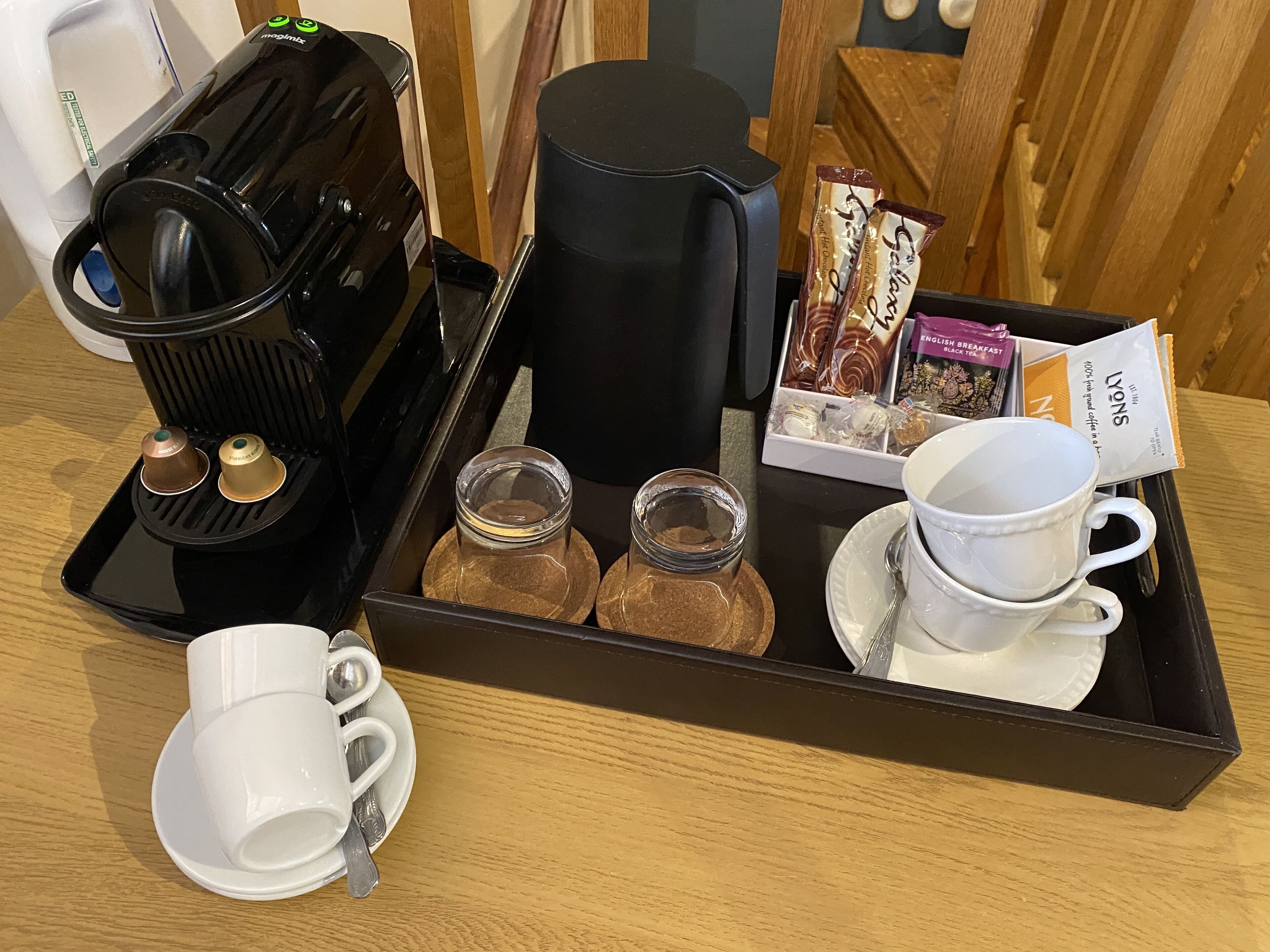 Una bandeja con cafetera, dos tazas, dos pequeños frascos, una bandeja de sobres de café y una tetera.