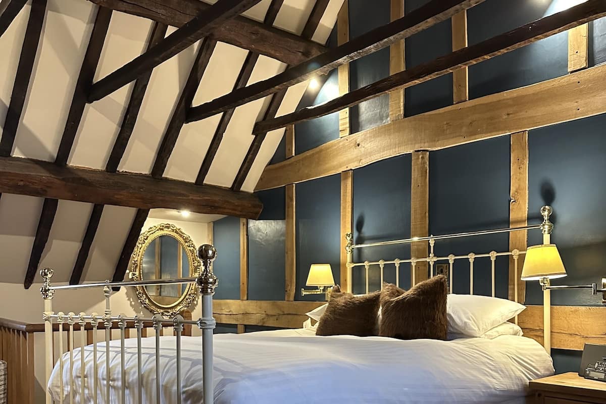 Un dormitorio con cama con dosel, vigas de madera en el techo y una mesita de noche con lámpara.
