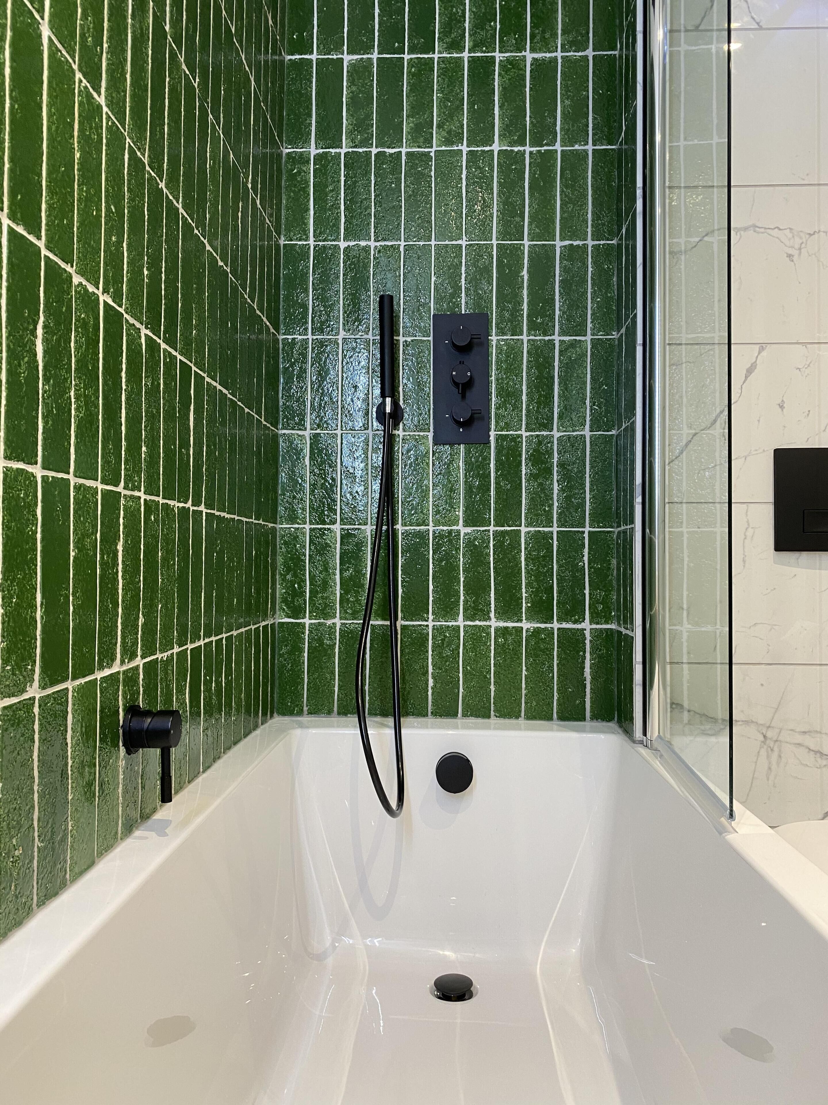 A bathtub with a showerhead, a control panel, and a drain.