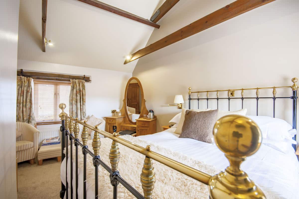 Un dormitorio con cama, mesita de noche, cómoda, espejo y ventana con cortinas.