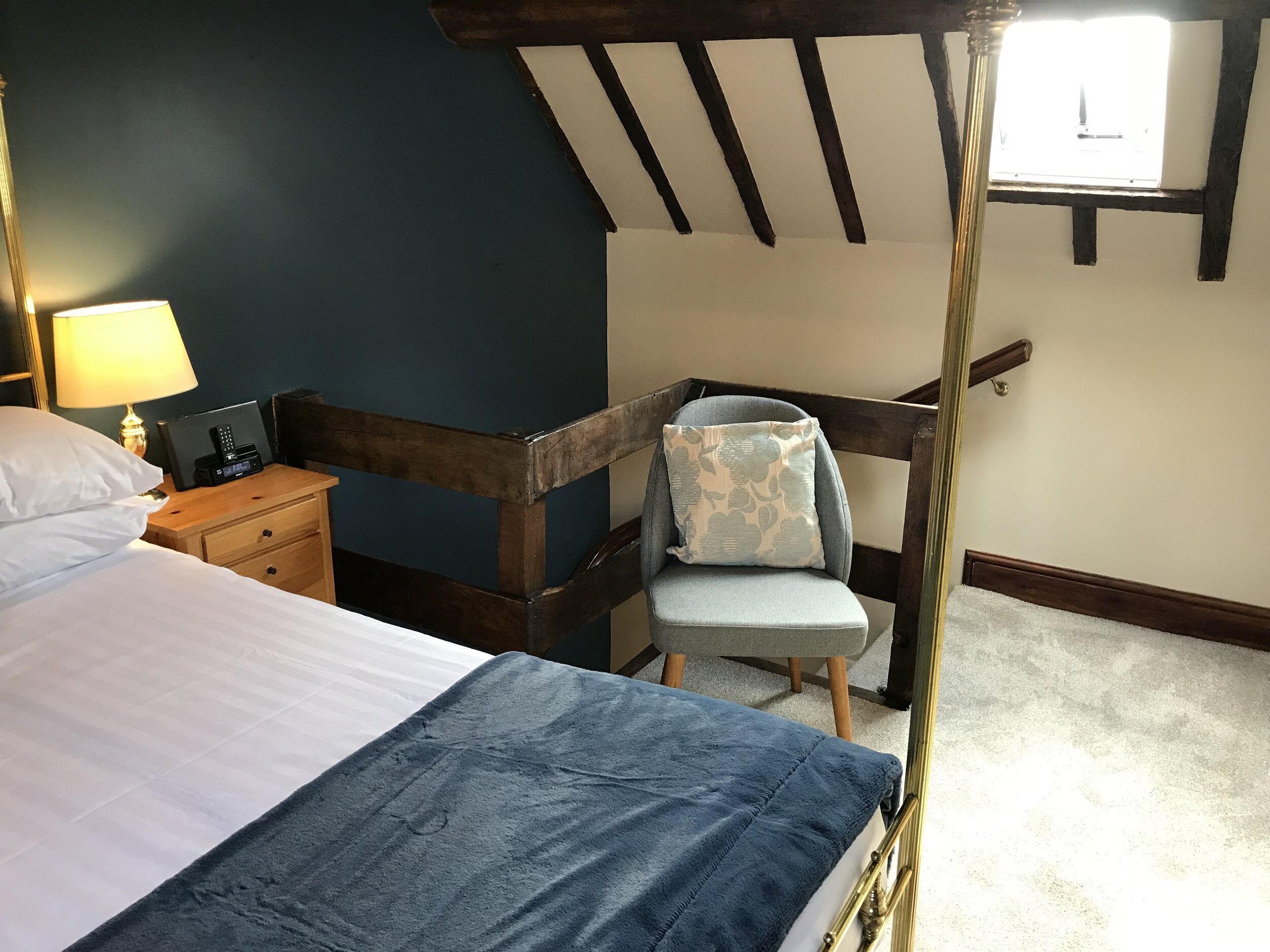 Un dormitorio con cama, mesita de noche, silla y ventana.
