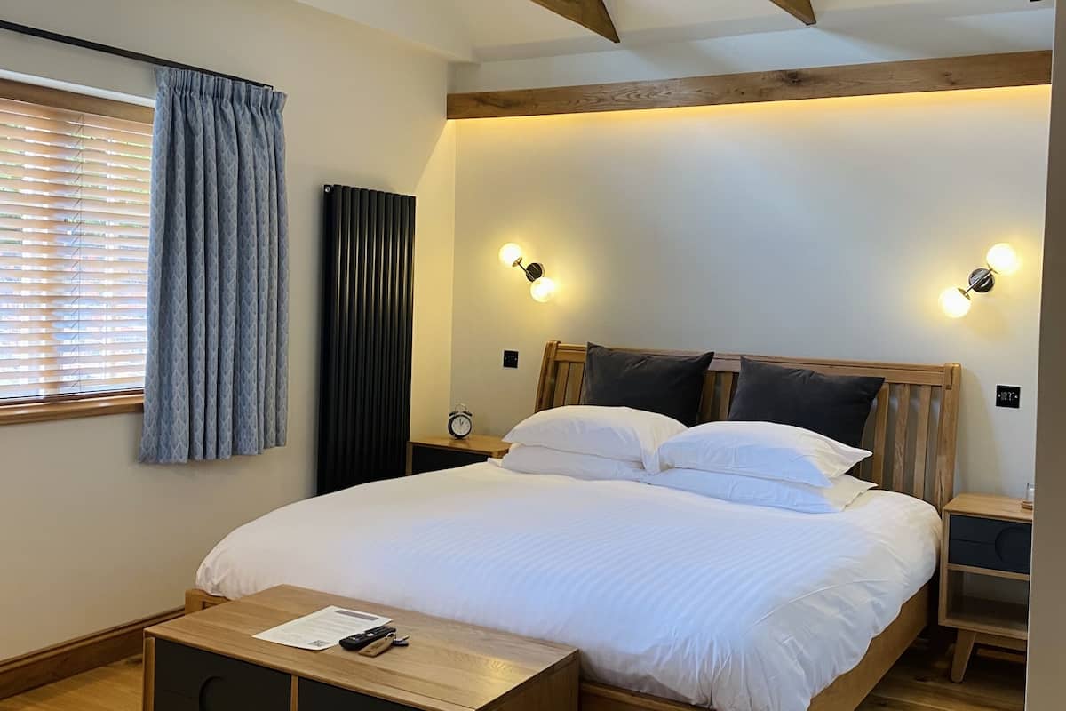 Un dormitorio con cama de madera, mesitas de noche, un banco de madera y una ventana con persianas.