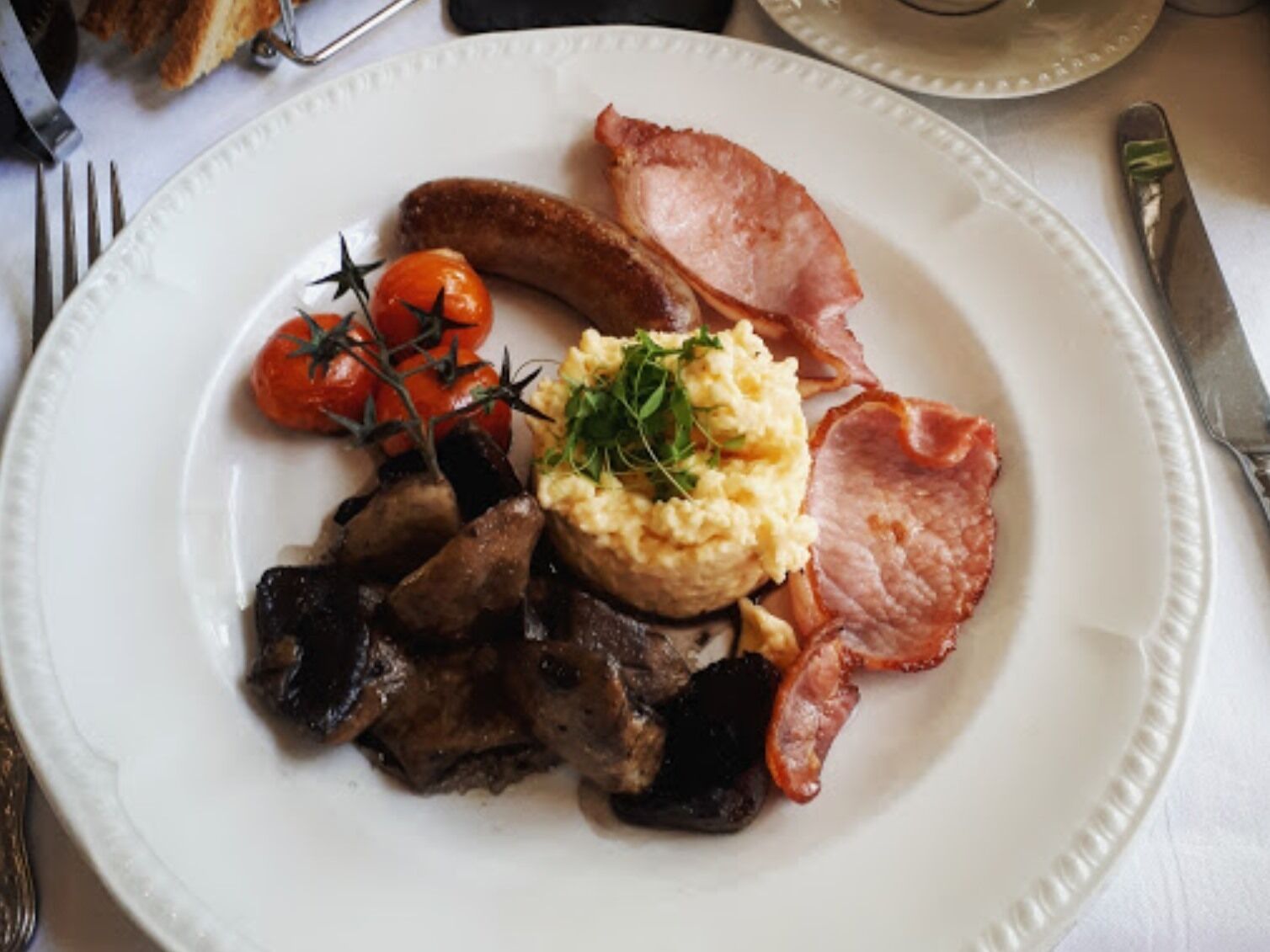 Une assiette contenant des œufs brouillés, du bacon, des saucisses, des champignons et des tomates cerises.