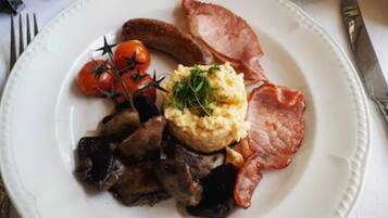 Une assiette contenant des œufs brouillés, du bacon, des saucisses, des champignons et des tomates cerises.