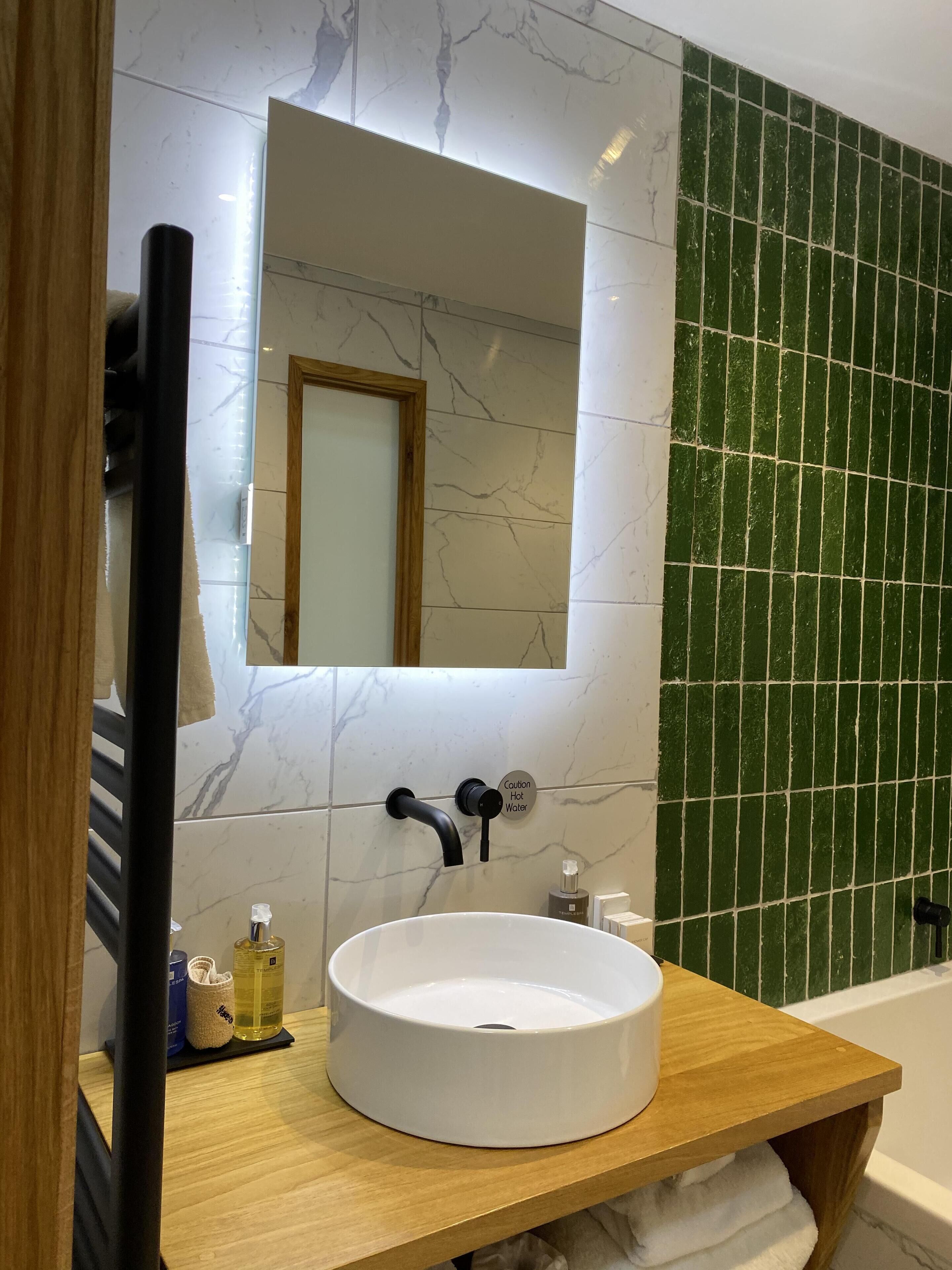 Un baño con lavamanos de mármol blanco, un espejo y un letrero de precaución para agua caliente.