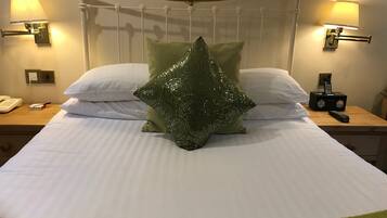 Una cama bien hecha con un cojín verde estampado, almohadas blancas y un plaid verde al pie. Hay dos mesitas de noche, una con lámparas y un teléfono.