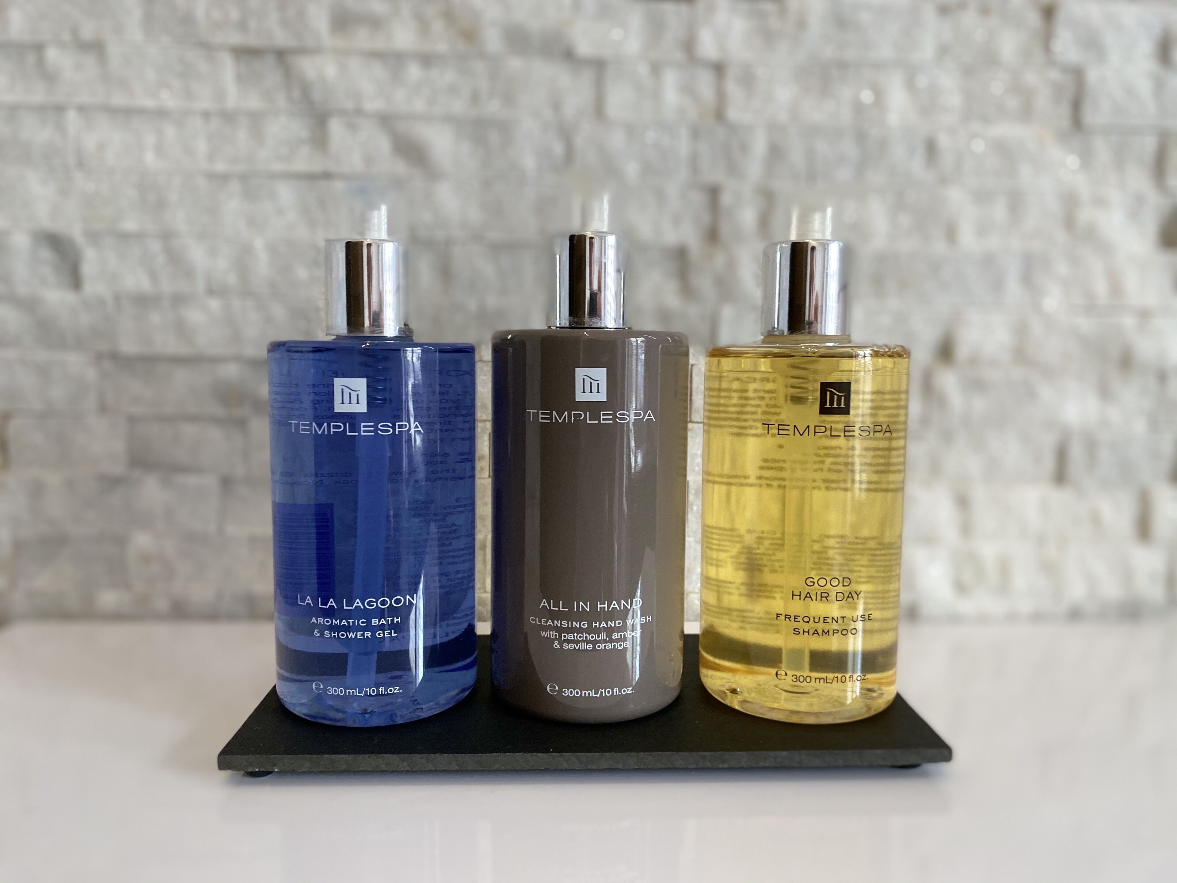 Drei Flaschen Templespa Produkte auf einem schwarzen Tablett vor einer strukturierten Wand.