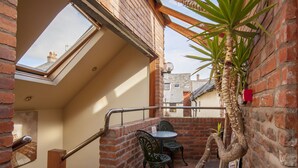 Un pequeño patio con pared de ladrillo, baranda de madera y una mesa con sillas.