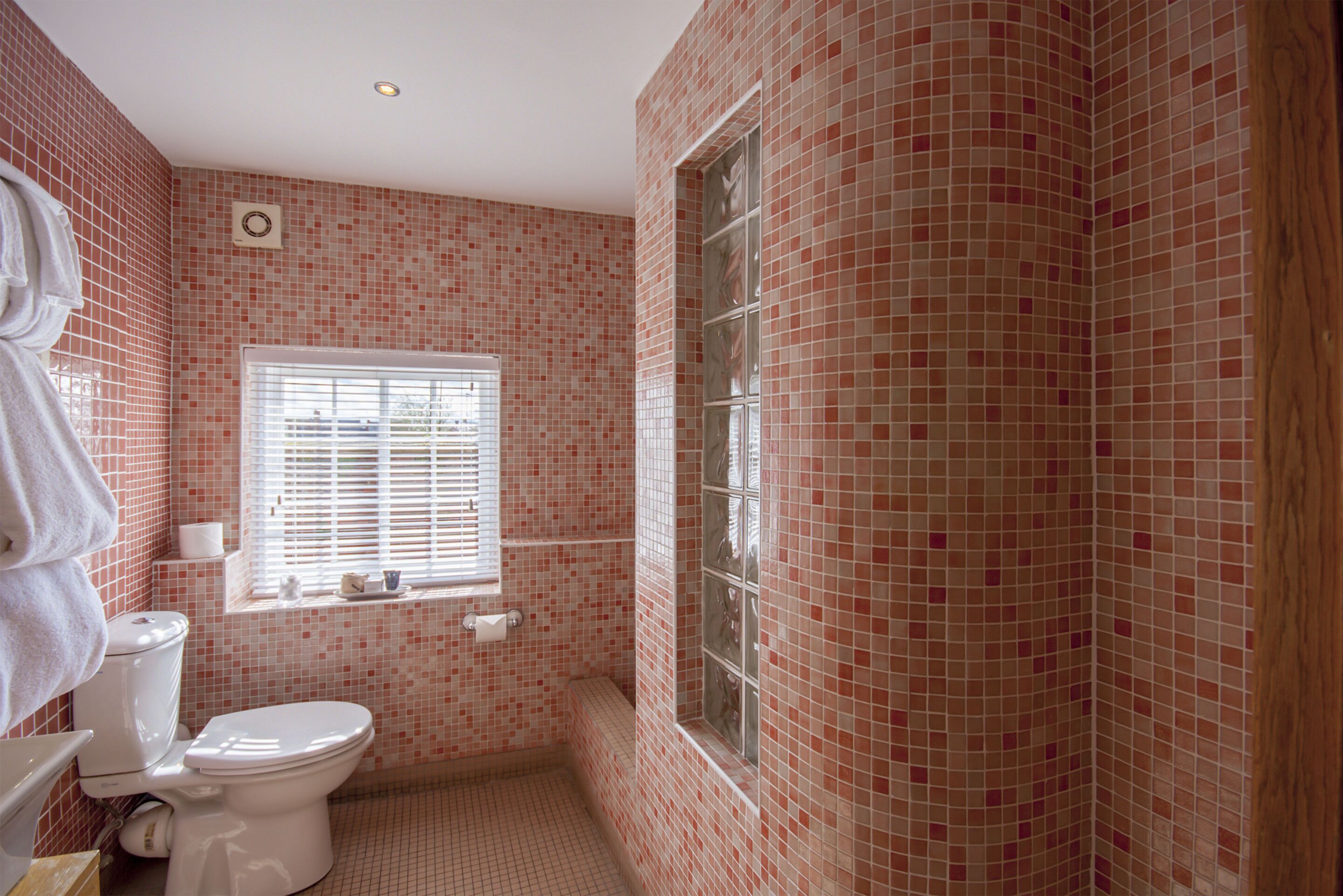 Une salle de bain avec des toilettes, une fenêtre et un mur carrelé.
