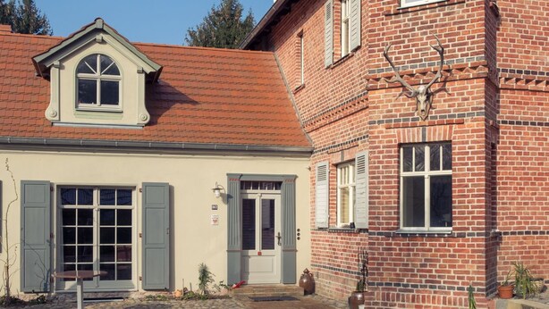 A two-story brick building with a tiled roof, a front door, and a small garden area with a gravel path. - Hermannsmühle (Treuenbrietzen)