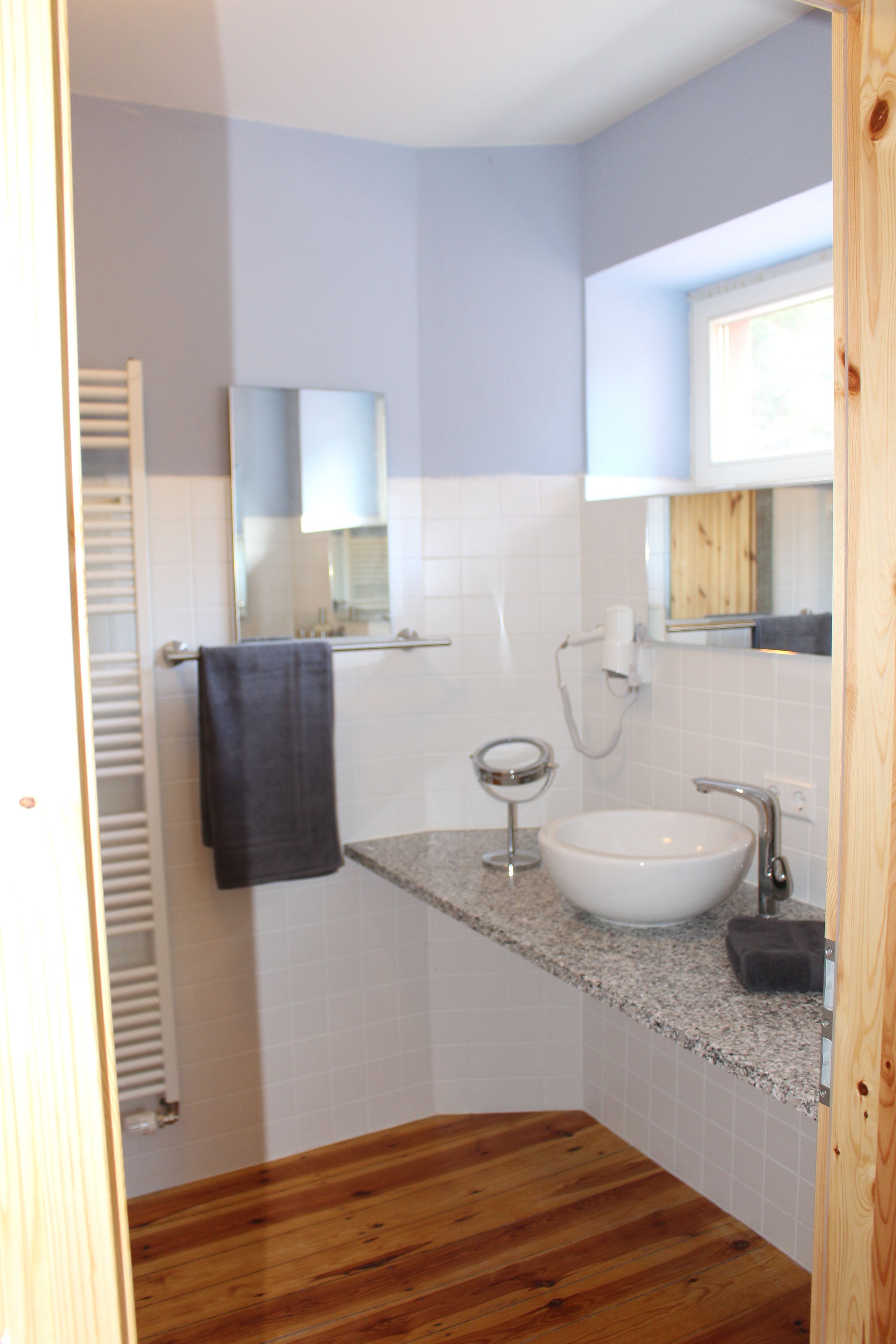 Un baño con tocador de madera, un lavamanos blanco, una toalla colgada en la pared y un espejo sobre el lavamanos.