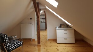 A loft-style room with a sloped ceiling, wooden beams, a white desk, a chair, and a bookshelf. - Hermannsmühle (Treuenbrietzen)