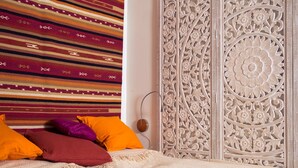 A bedroom with a patterned wall hanging, a decorative headboard, and a bed with a textured cover. - Hermannsmühle (Treuenbrietzen)