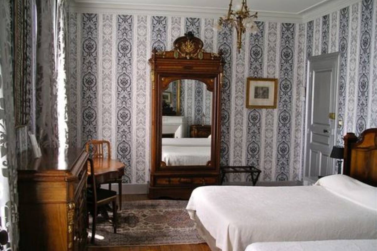 Een slaapkamer met twee bedden, een houten dressoir, een stoel en een grote spiegel.