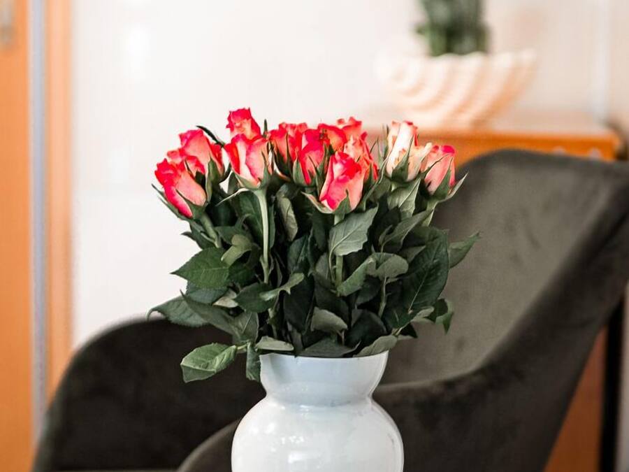 A white vase with red and pink flowers on a table.