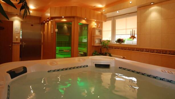 Een spa-ruimte met een bubbelbad, houten wanden en een raam met bloemen.