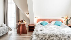 Een hotelkamer met twee bedden, een houten nachtkastje met een schaal fruit, een nachtkastje en een vaas met bloemen.