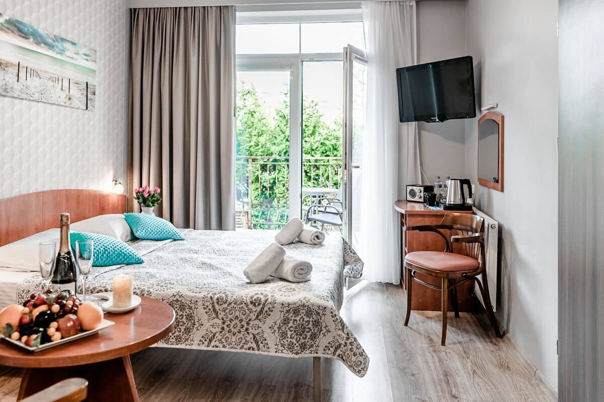 Habitación de hotel con cama, escritorio, silla, televisor y balcón con vistas.