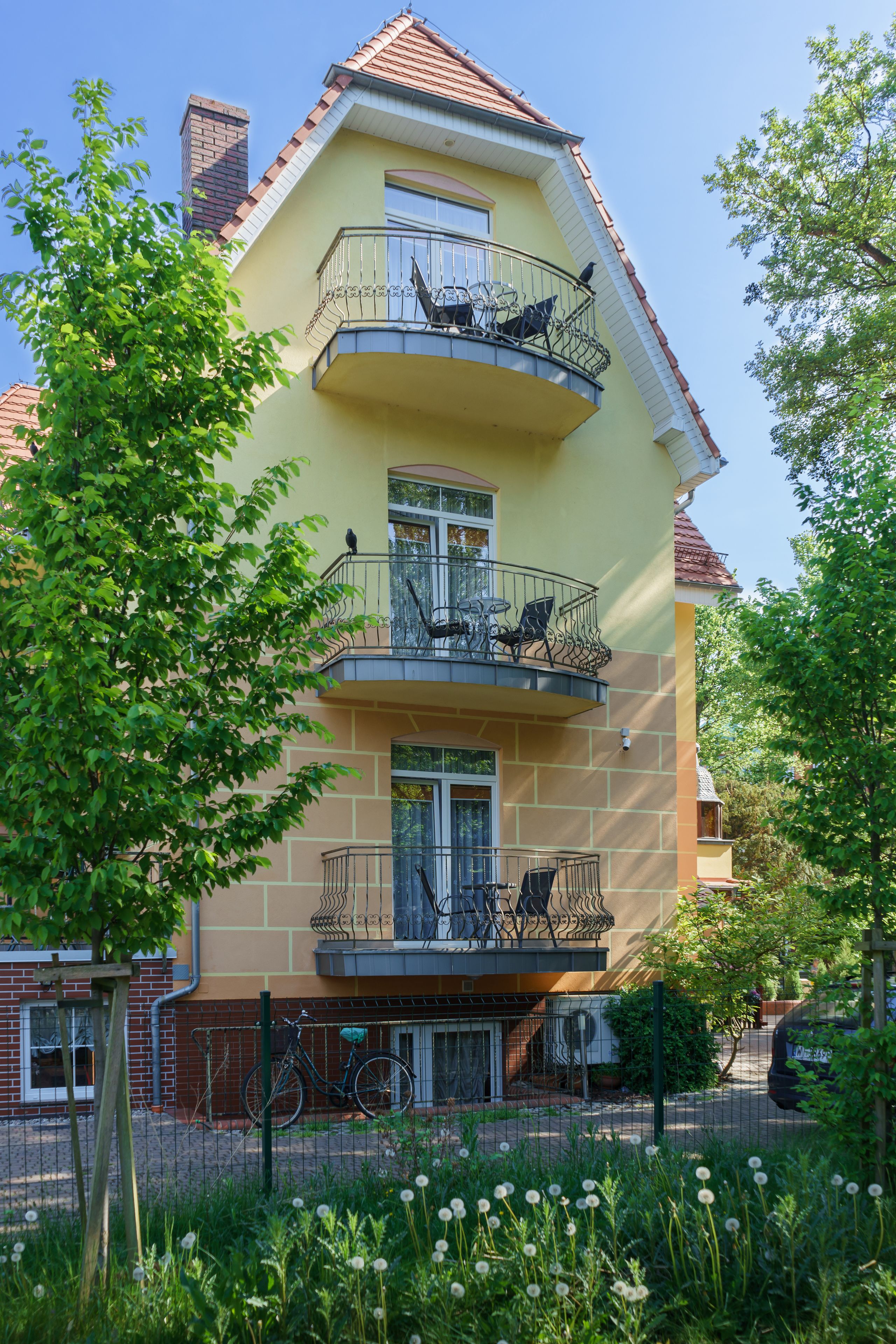A two-story building with a balcony on the upper floor, a bicycle parked outside, and a fence in the foreground.