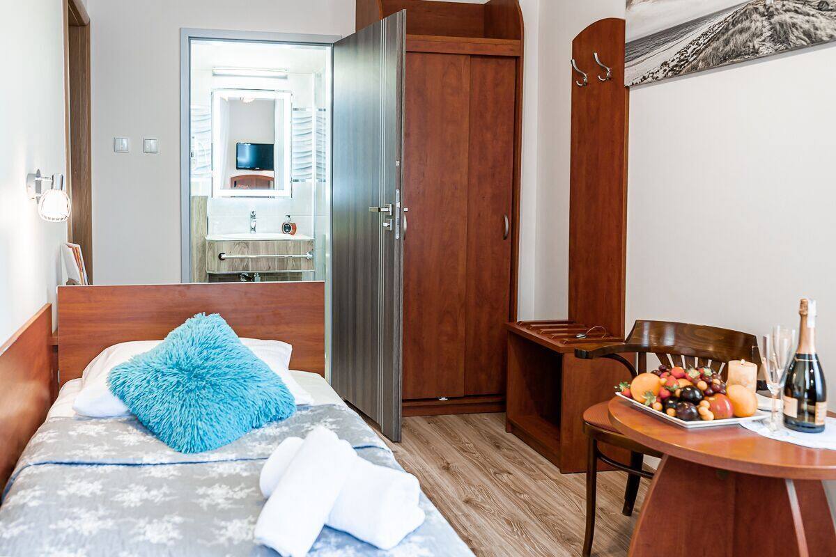 Habitación de hotel con una cama, un armario de madera, una mesita con una bandeja de frutas y una botella, y un espejo al fondo.