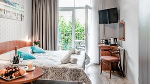 Hotelkamer met een bed, een bureau, een stoel, een televisie en een balkon met uitzicht op groen.