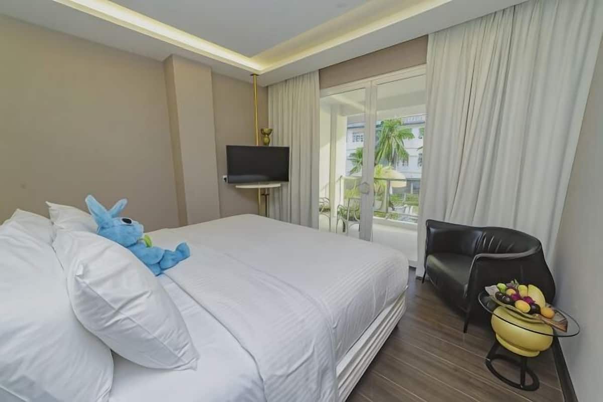 A hotel room with a bed, a TV, a chair, and a table with fruit.