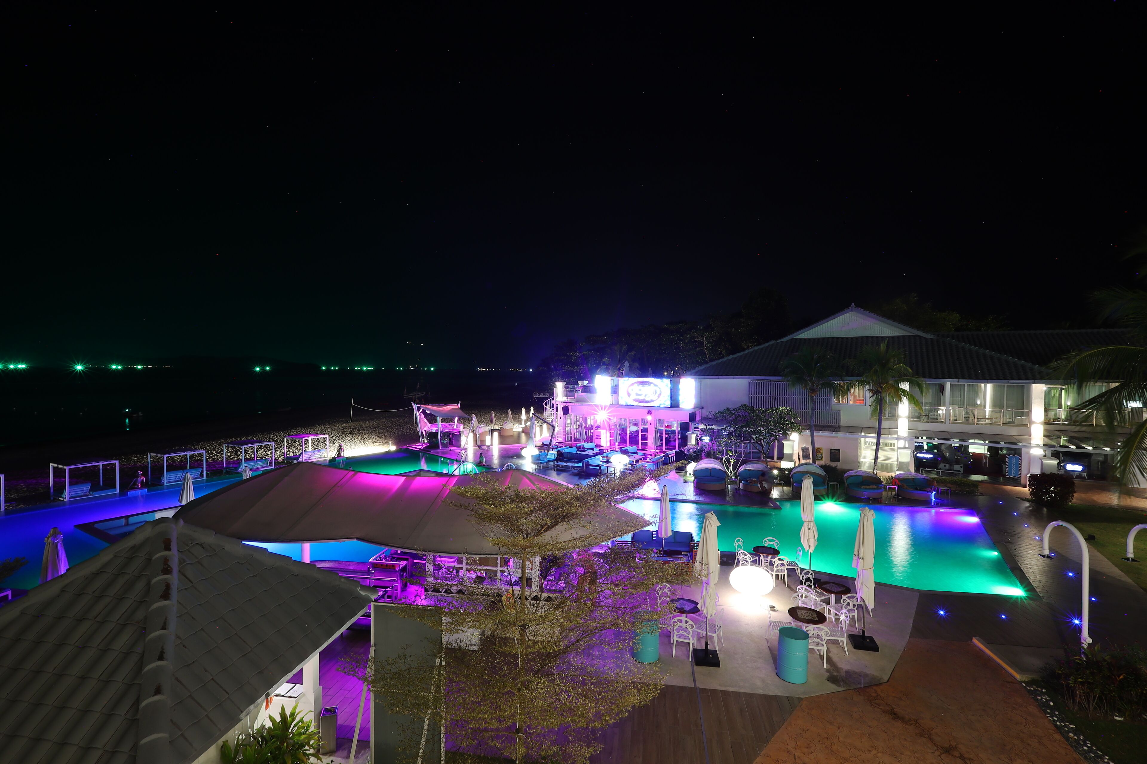 A nighttime view of a resort with a swimming pool, outdoor seating, and a building with illuminated signage.