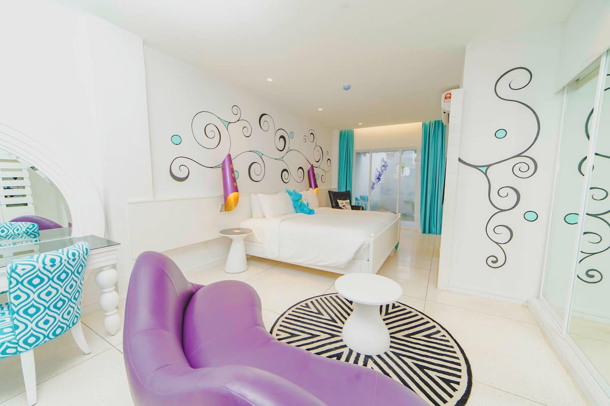 A modern hotel room with a bed, a purple chair, a small white table, and decorative wall art.