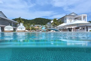 A swimming pool with a bridge, palm trees, and a mountain in the background.